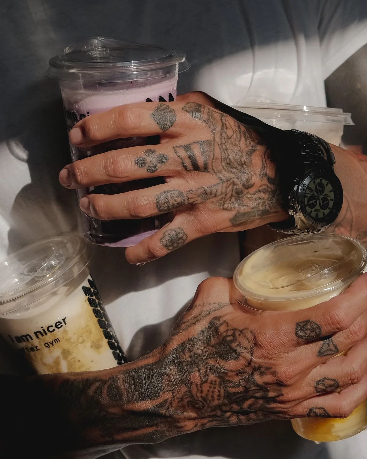 Tattooed hands holding four ASAI GYM smoothies