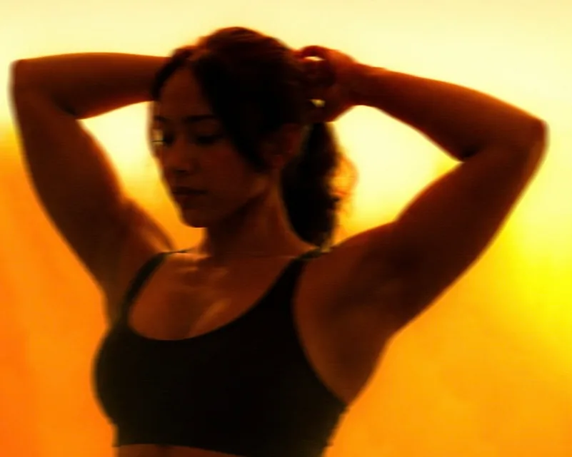 A member with her hands behind her head, silhouetted against the amber light of ASAI GYM